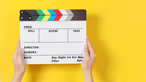 hands holding a clapperboard behind a bright yellow backdrop