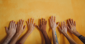 yellow wall, with seven hands touching the wall, all different backgrounds and races, showing diversity