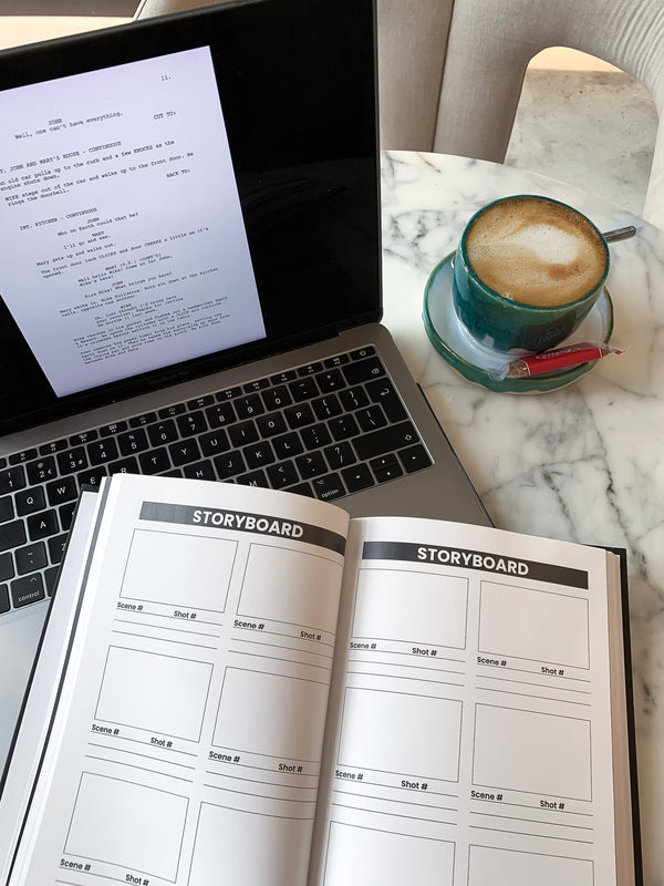 Marble table, with a coffee mug, an open MacBook Air laptop, and the storyboard page open from the beginner filmmaking planner