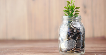 Oak wood background, with a jar full of pennies and coins, with a plant coming out of the top